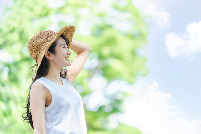 麦わら帽子をかぶり青空に笑いかけている女性の画像